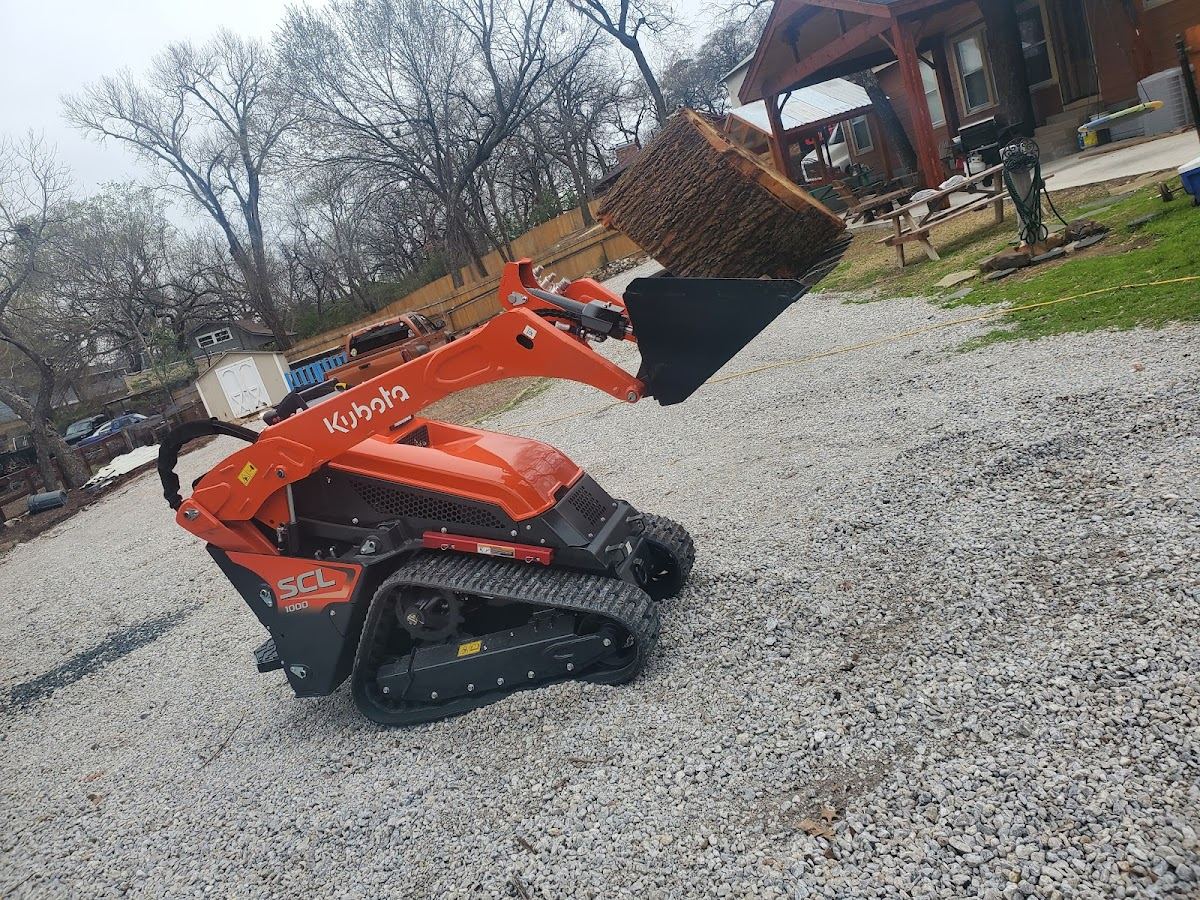 Kubota compact track loader carrying a hay bale across a gravel Texas property
